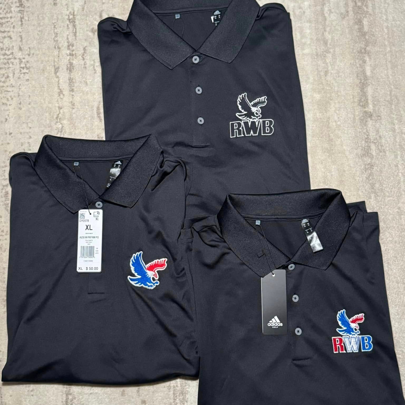 Three folded black polo shirts with RWB logo embroidered