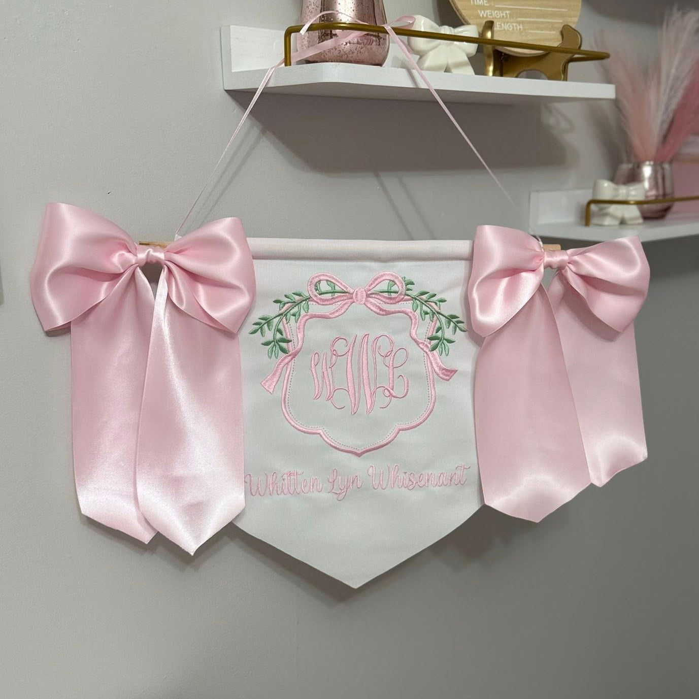 Decorative banner with pink ribbons and embroidered design on a plain background
