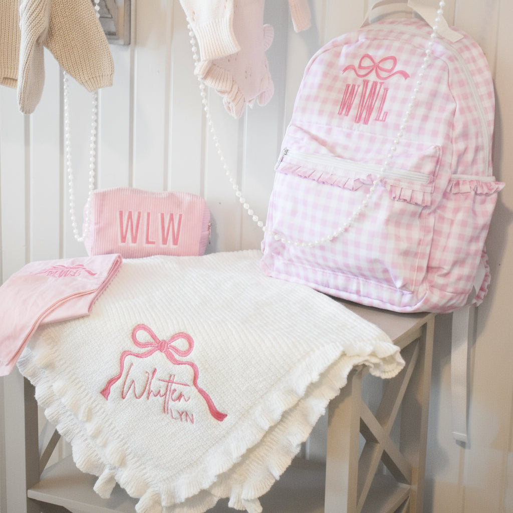 Pink checkered bag and blanket with 'WLW' initials on a chair against a wooden wall.
