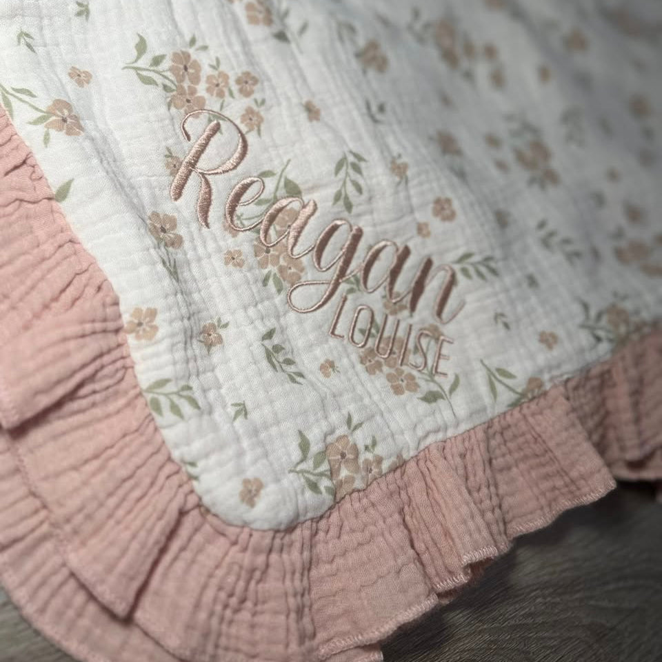 Floral-patterned blanket with embroidered name 'Reagan Louise' on a pink background
