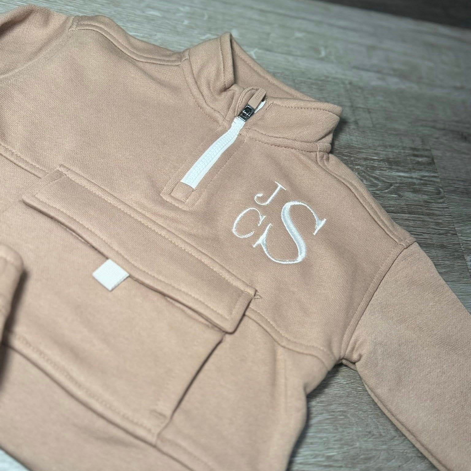 Brown fleece pullover with 'JCS' monogram on a wooden surface