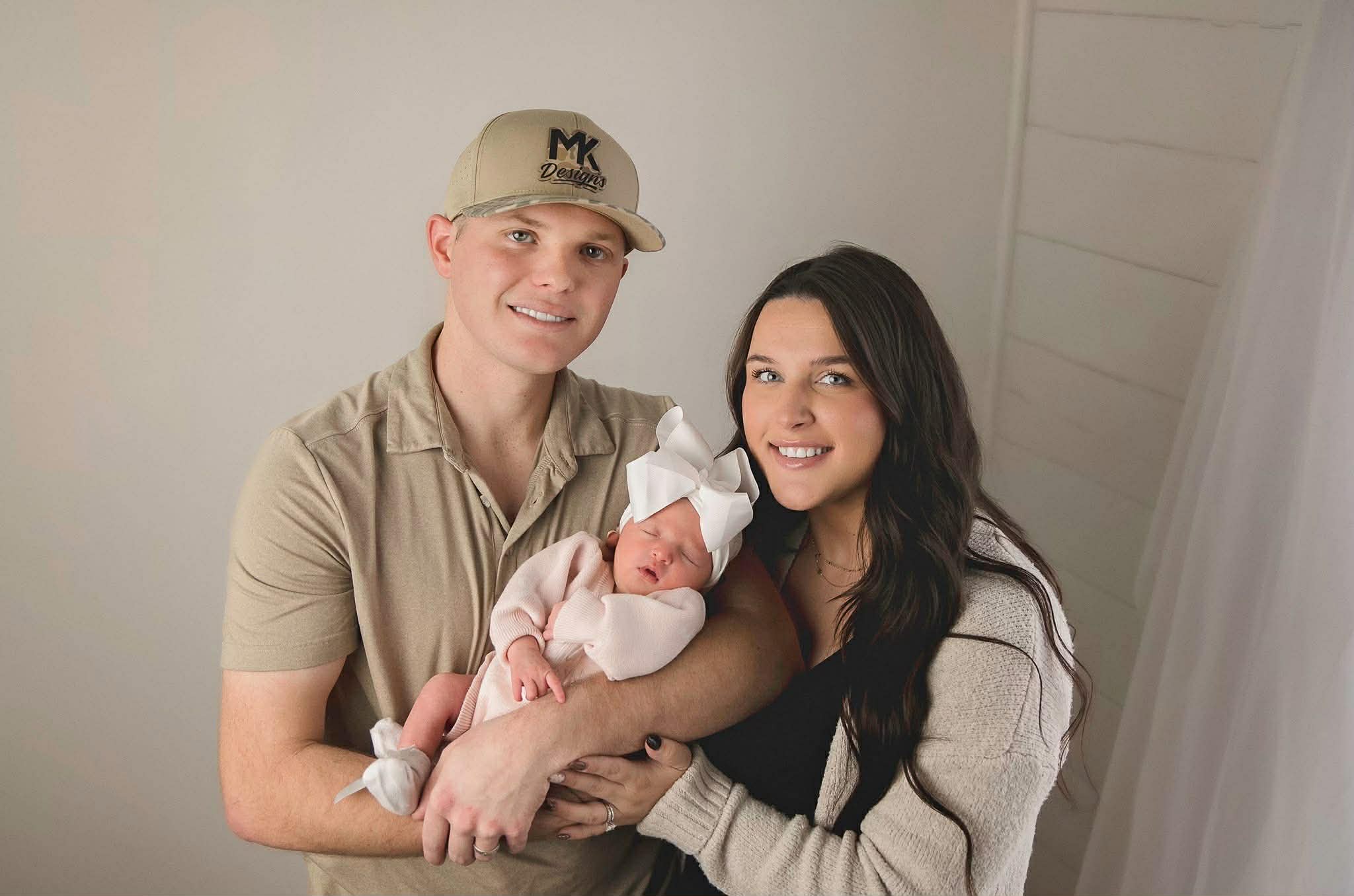 Husband & wife holding their new baby; husband is wearing MK Designed embroidered hat